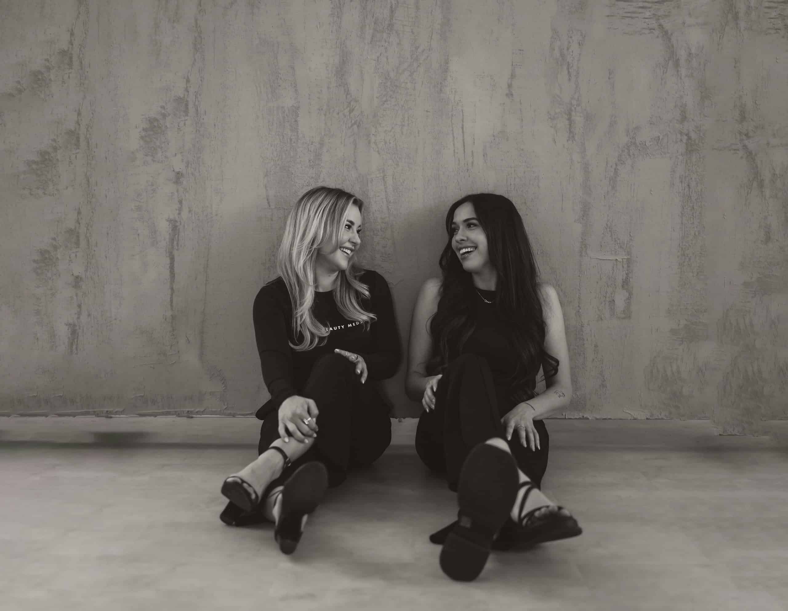 Two women sitting on the floor, smiling together.