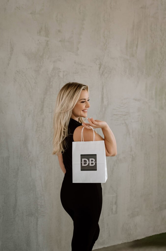 Woman smiling, holding branded shopping bag.