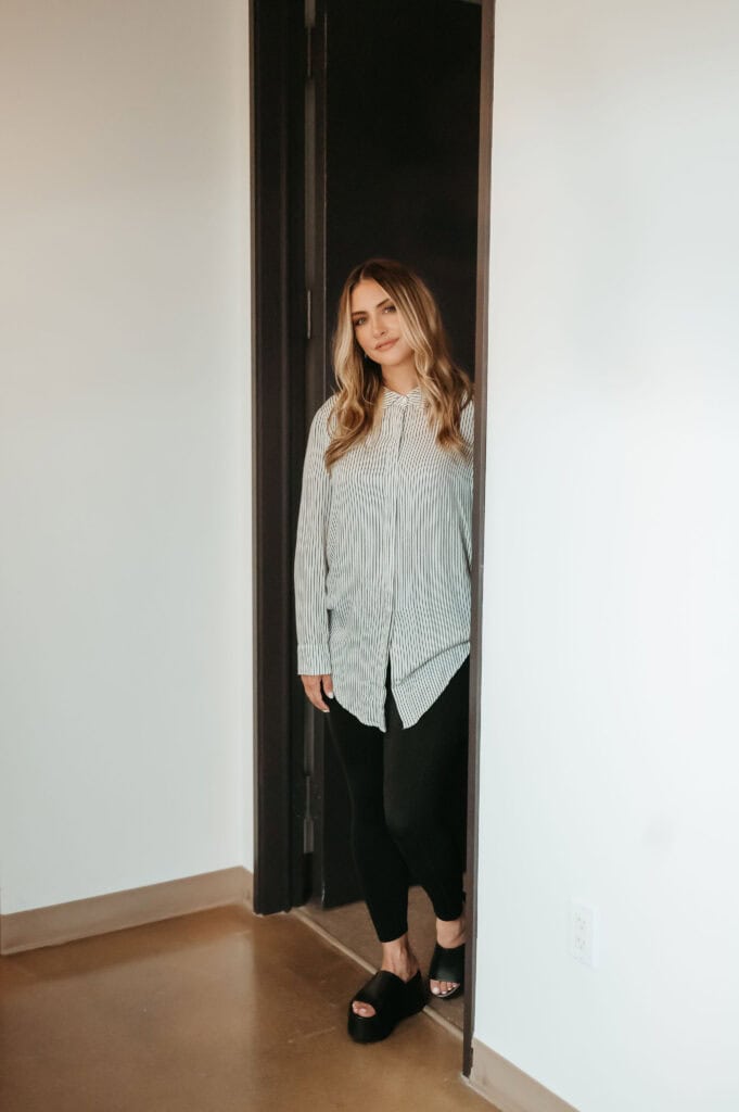 Woman standing in doorway, casual outfit, neutral expression.